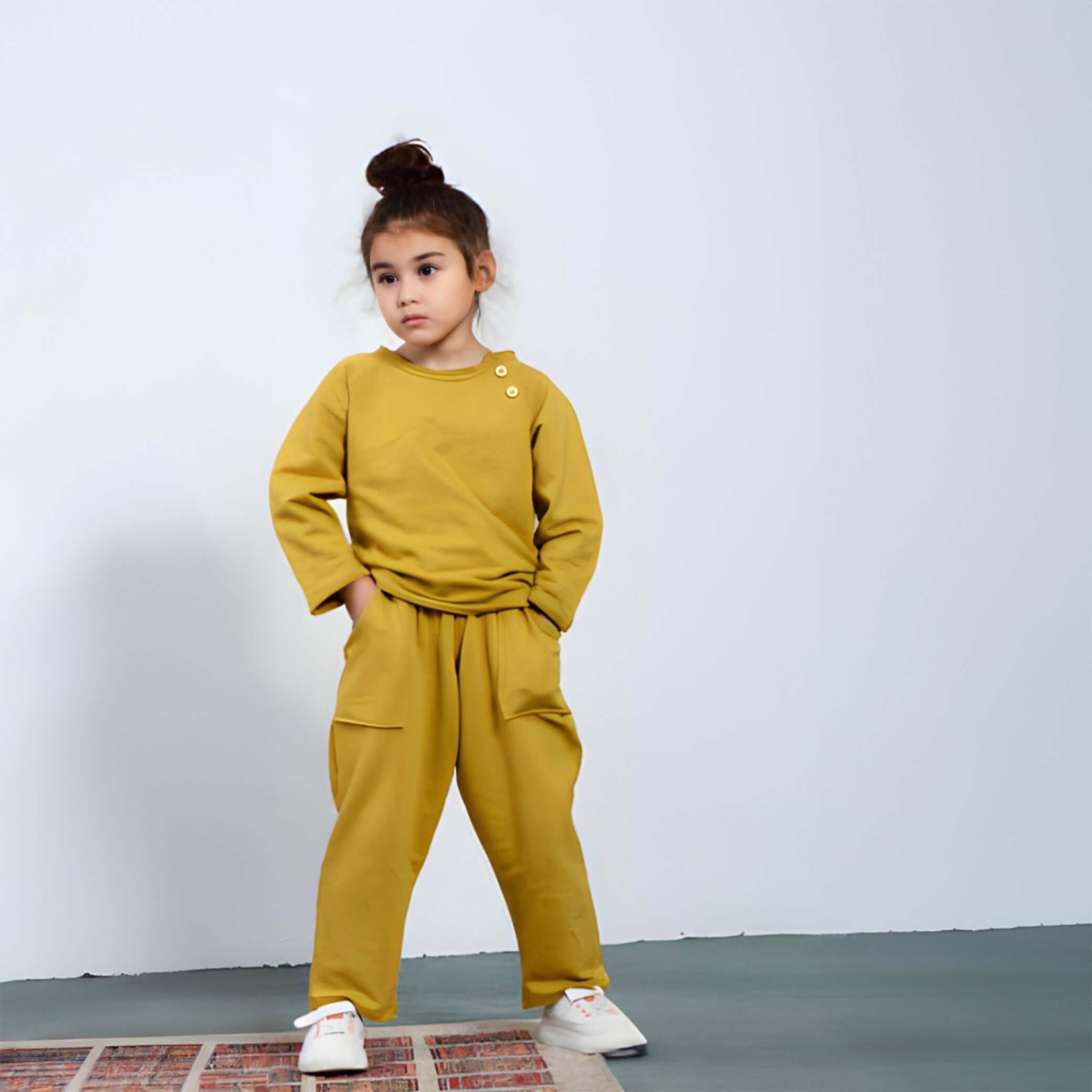 Das Kindermodell trägt ein 2-teiliges Set Ober- und Unterteil im Senf