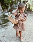 ein kleines Mädchen mit einem Korb, das ein Nehir Kleid aus Bio-Baumwolle trägt
