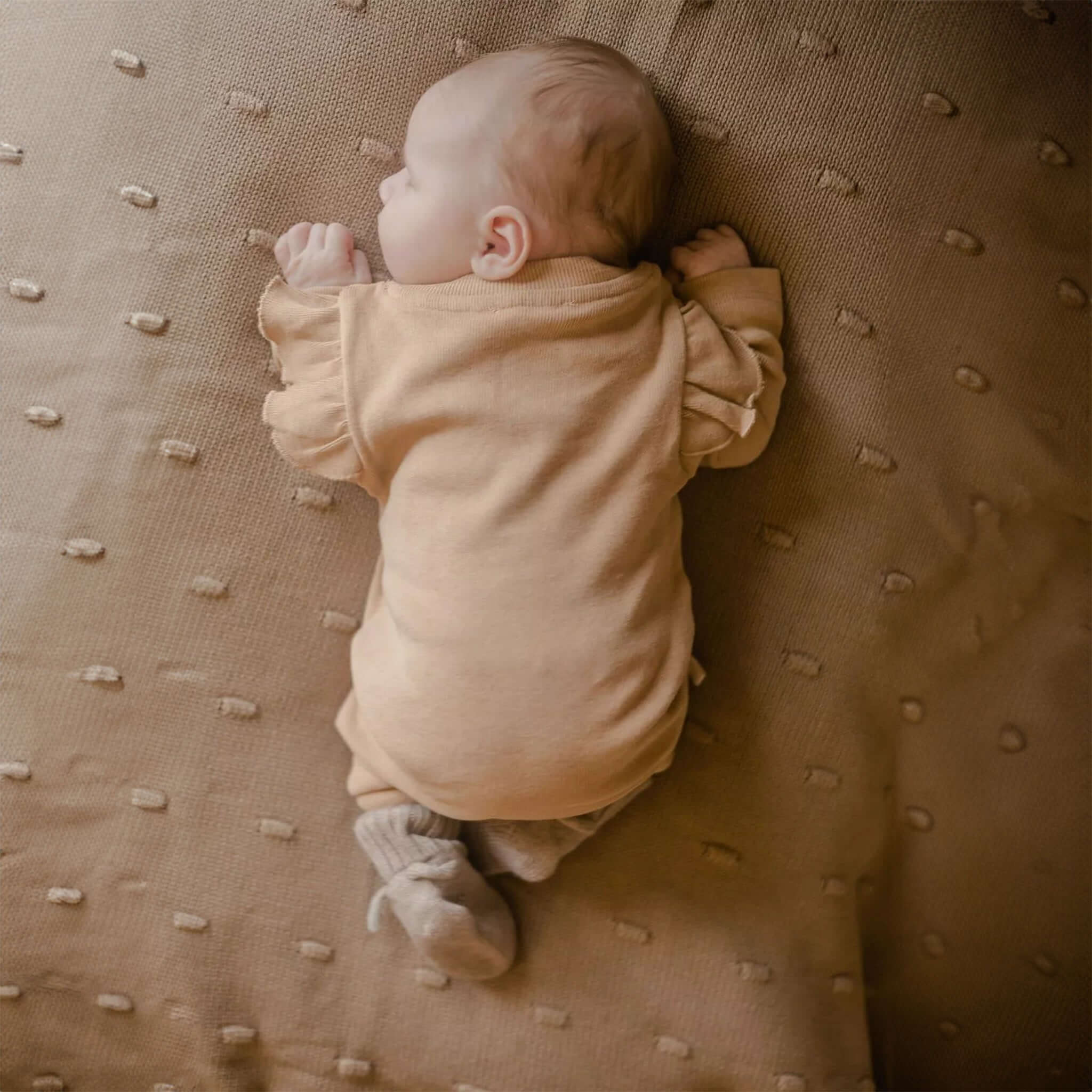Ein schlafendes Baby, das Hausschuhe aus Merinowolle in Creme trägt