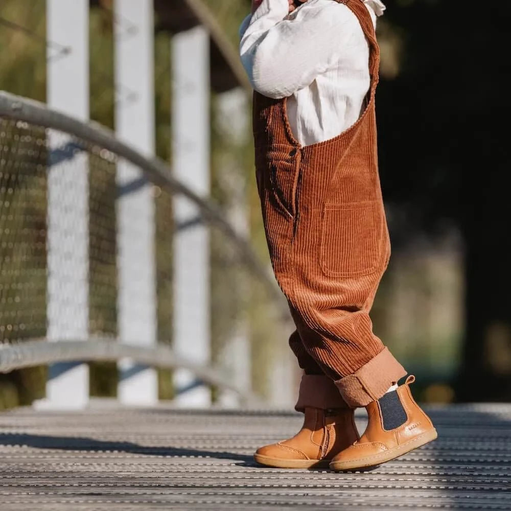 ein Kind, das Axelle Lauflernschuhe in Braun /Marine trägt