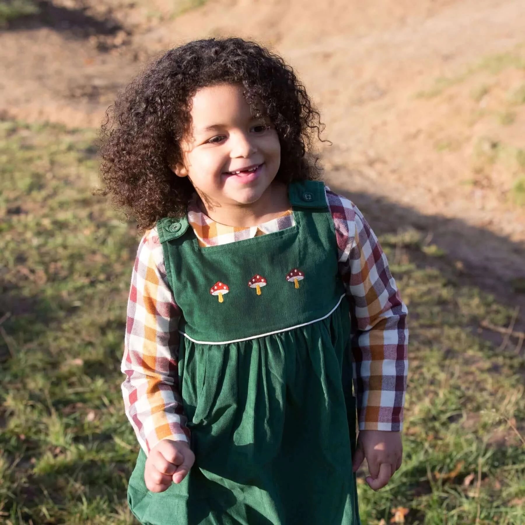 Glückliches Kind trägt Besticktes Toadstool Cord Pinny Kleid