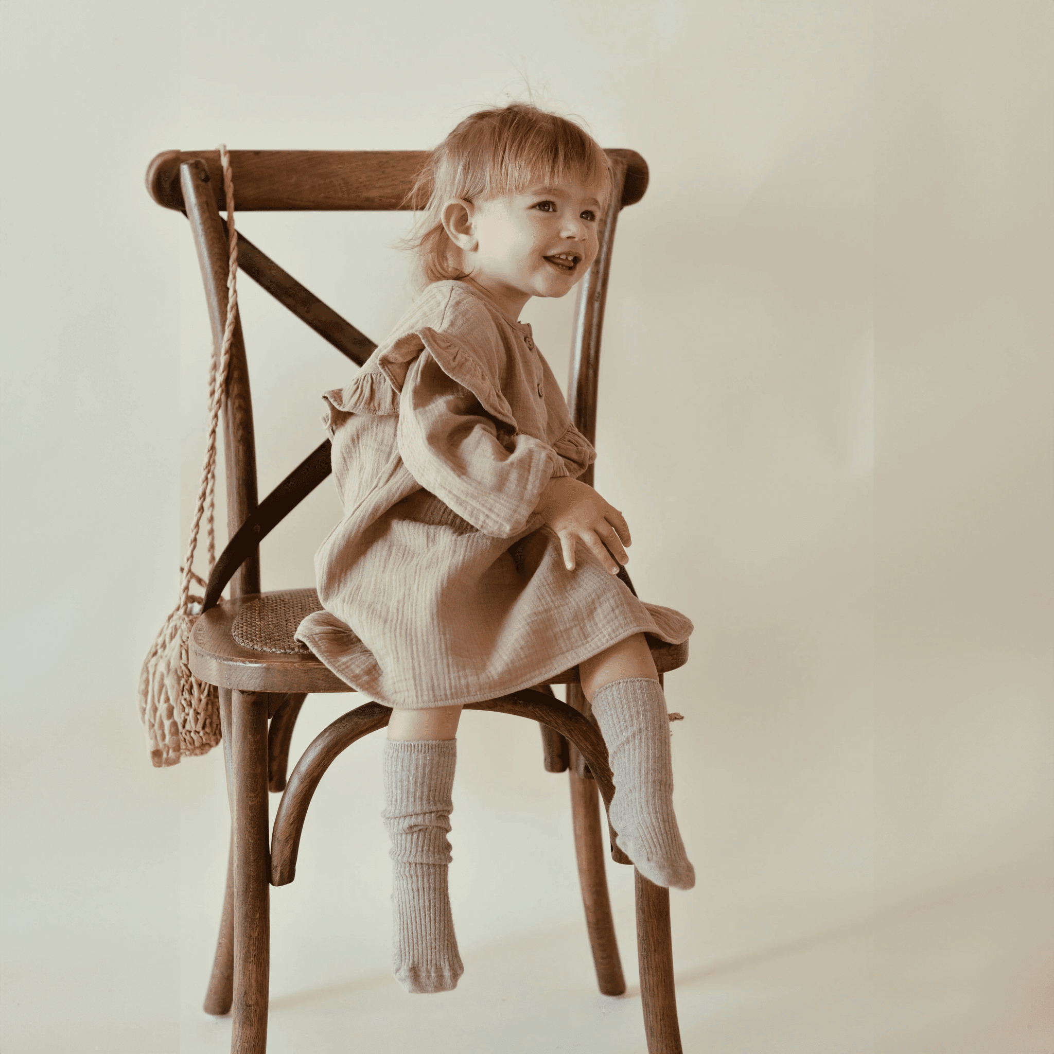 &quot;Ein fröhliches Mädchen sitzt auf dem Stuhl und trägt ein Nehir Kleid aus Bio-Baumwolle.&quot;