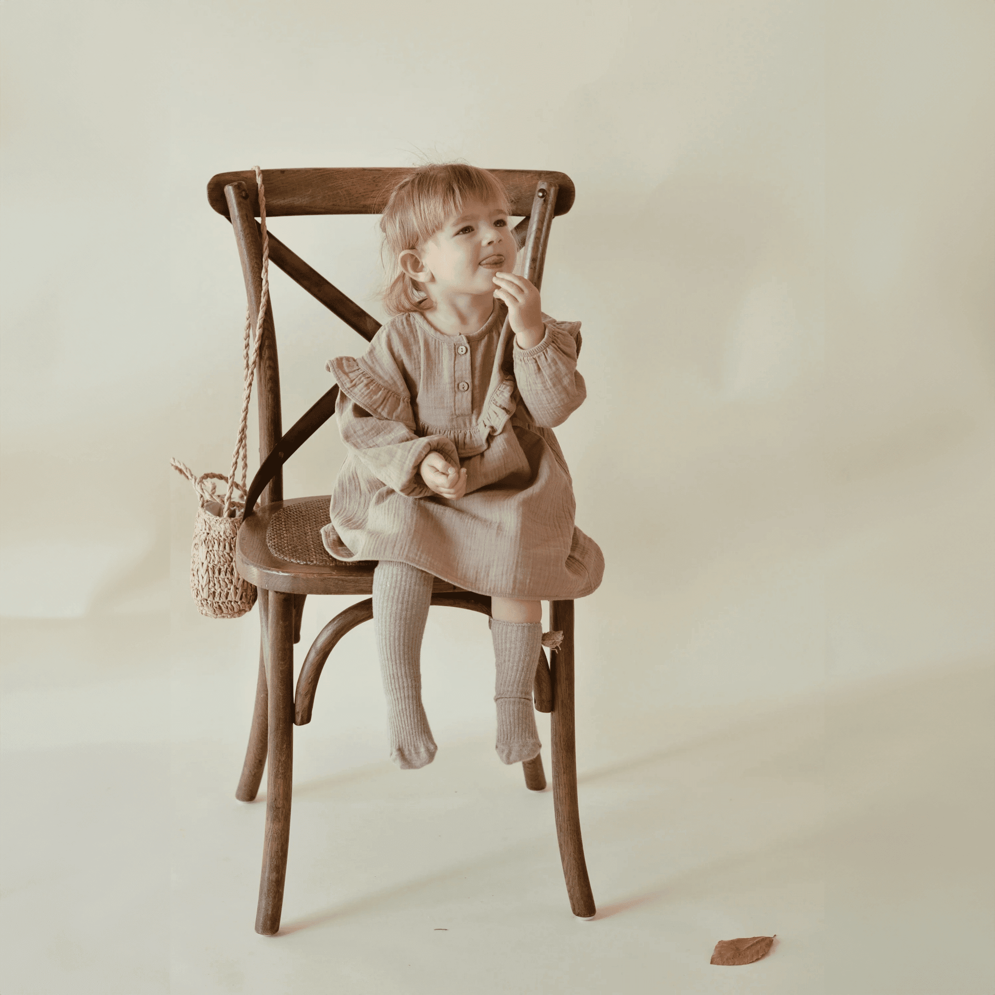 Ein süßes Mädchen sitzt auf dem Stuhl und trägt ein Nehir Kleid aus Bio-Baumwolle