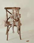 Ein süßes Mädchen sitzt auf dem Stuhl und trägt ein Nehir Kleid aus Bio-Baumwolle